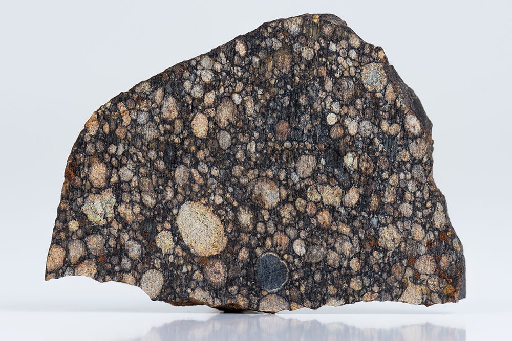 Météorite chondrite brute noir et gris — fragment cosmique 4,56 milliards d'années, histoire depuis la nébuleuse solaire primordiale